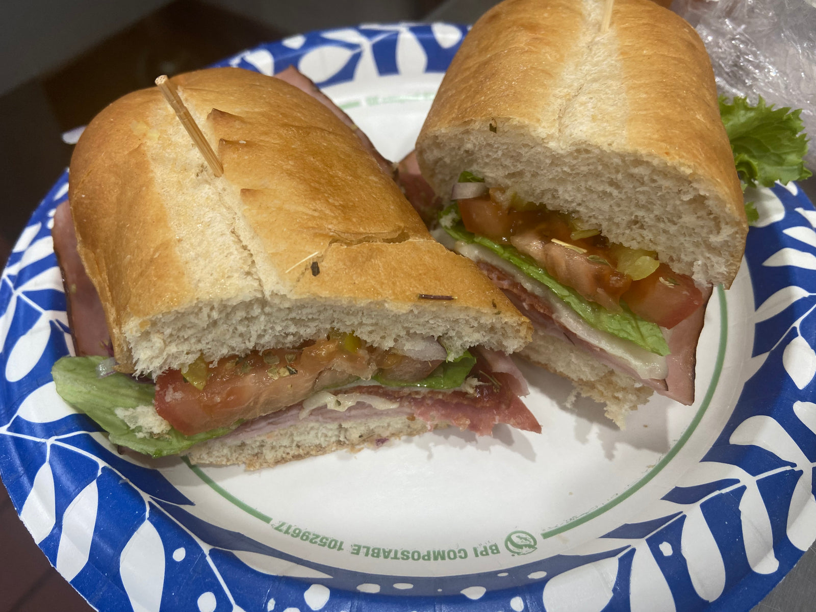 An Italian sub cut in half, layered with ham, salami, cheese, lettuce and tomato
