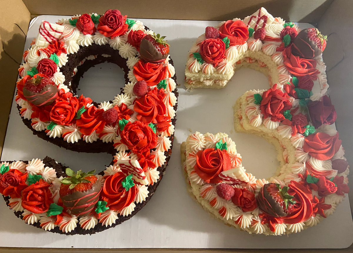 A custom number cake shaped as 93, covered in red buttercream roses, piped stars and chocolate-dipped strawberries
