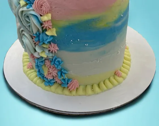 A pastel birthday cake with pink, blue and yellow buttercream