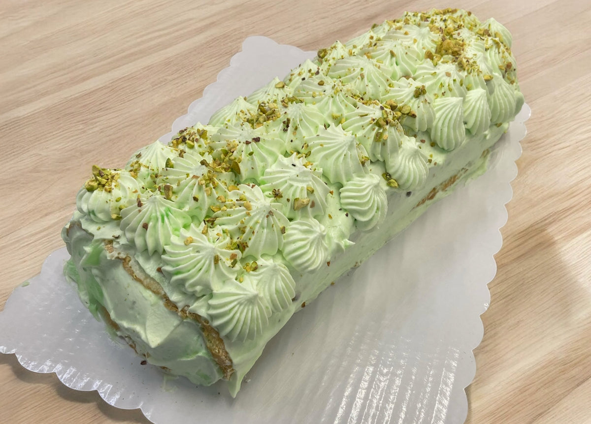 A roll cake piped with pale green cream and chopped pistachios